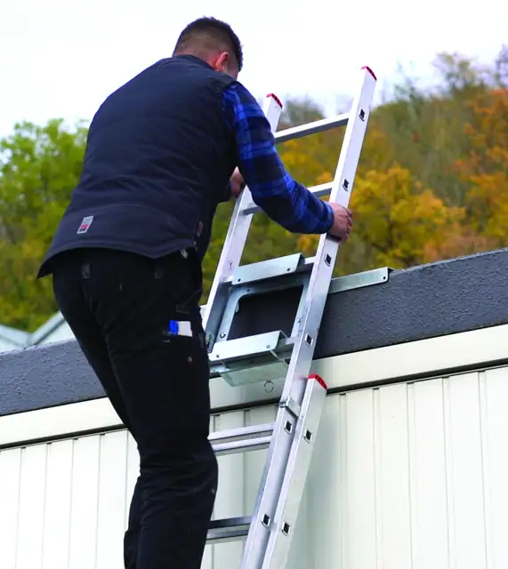 Handwerker steigt auf einer Anlegeleiter zum Flachdach hinauf, die Leiter ist oben mit WeMa-Step Flachdachschienen an der Dachkante gesichert