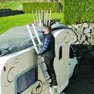 Mann steigt auf einer Anlegeleiter zum Dach eines Wohnmobils hinauf, die Leiter ist oben mit WeMa-Step Flachdachschienen gesichert