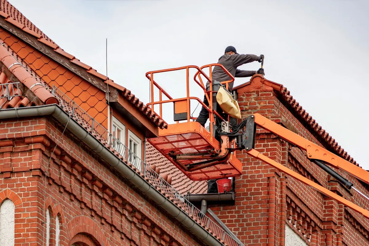 Dachdecker im Korb eines Hubsteigers arbeitet am Dach eines hohen Backsteinhauses