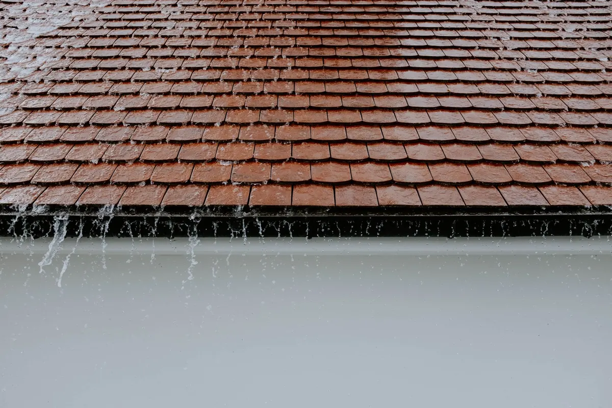 Regenwasser läuft über die Kante einer vollen Dachrinne an einem Ziegeldach